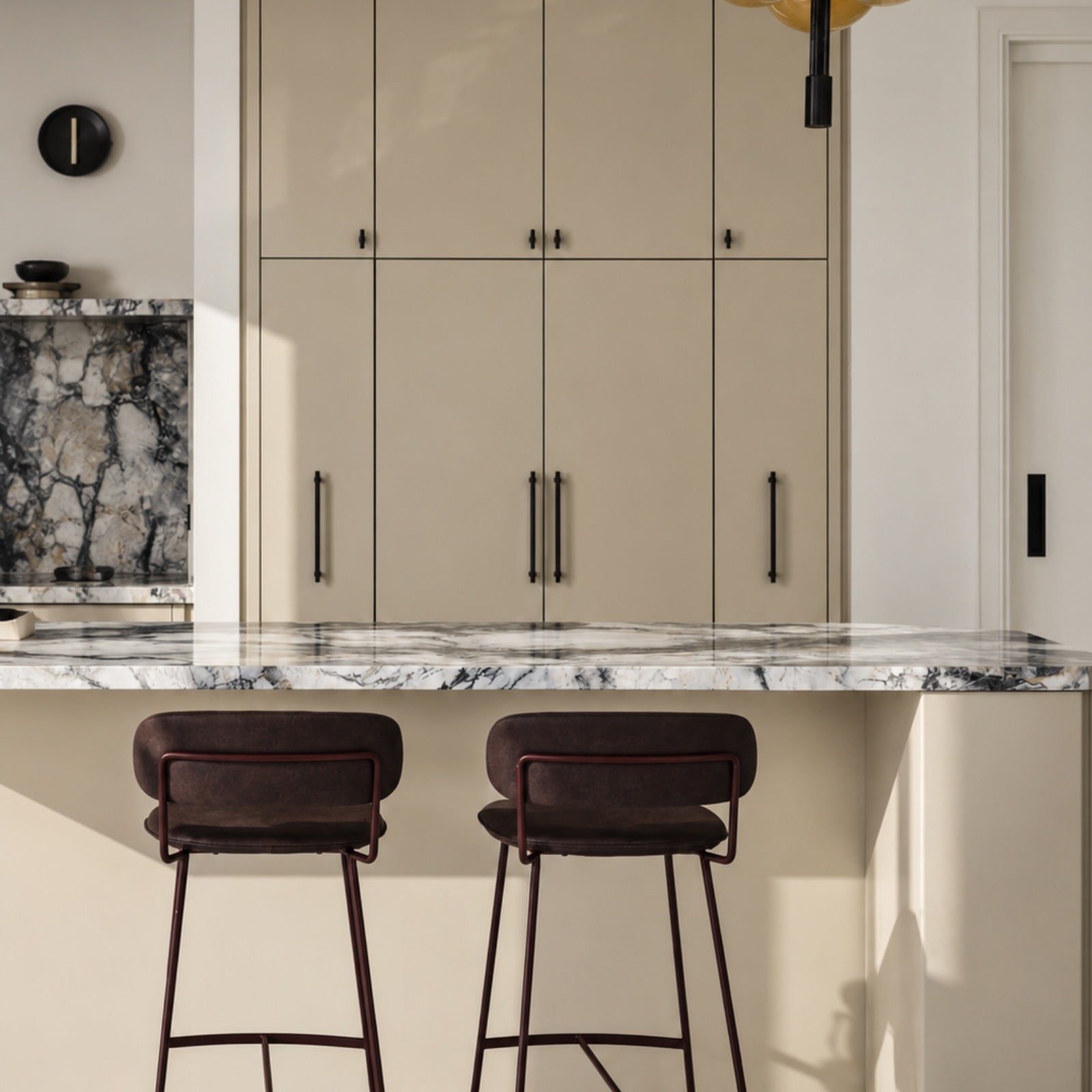 A modern kitchen interior with beige cabinets, a white marble countertop, and two dark brown bar stools in the foreground.